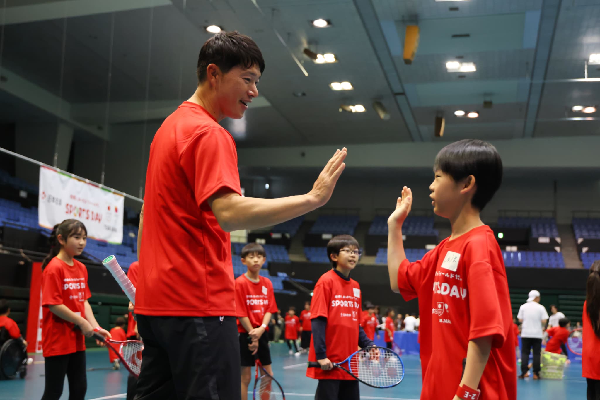 テニス体験で参加者とハイタッチをする近藤プロ（写真：アフロスポーツ）